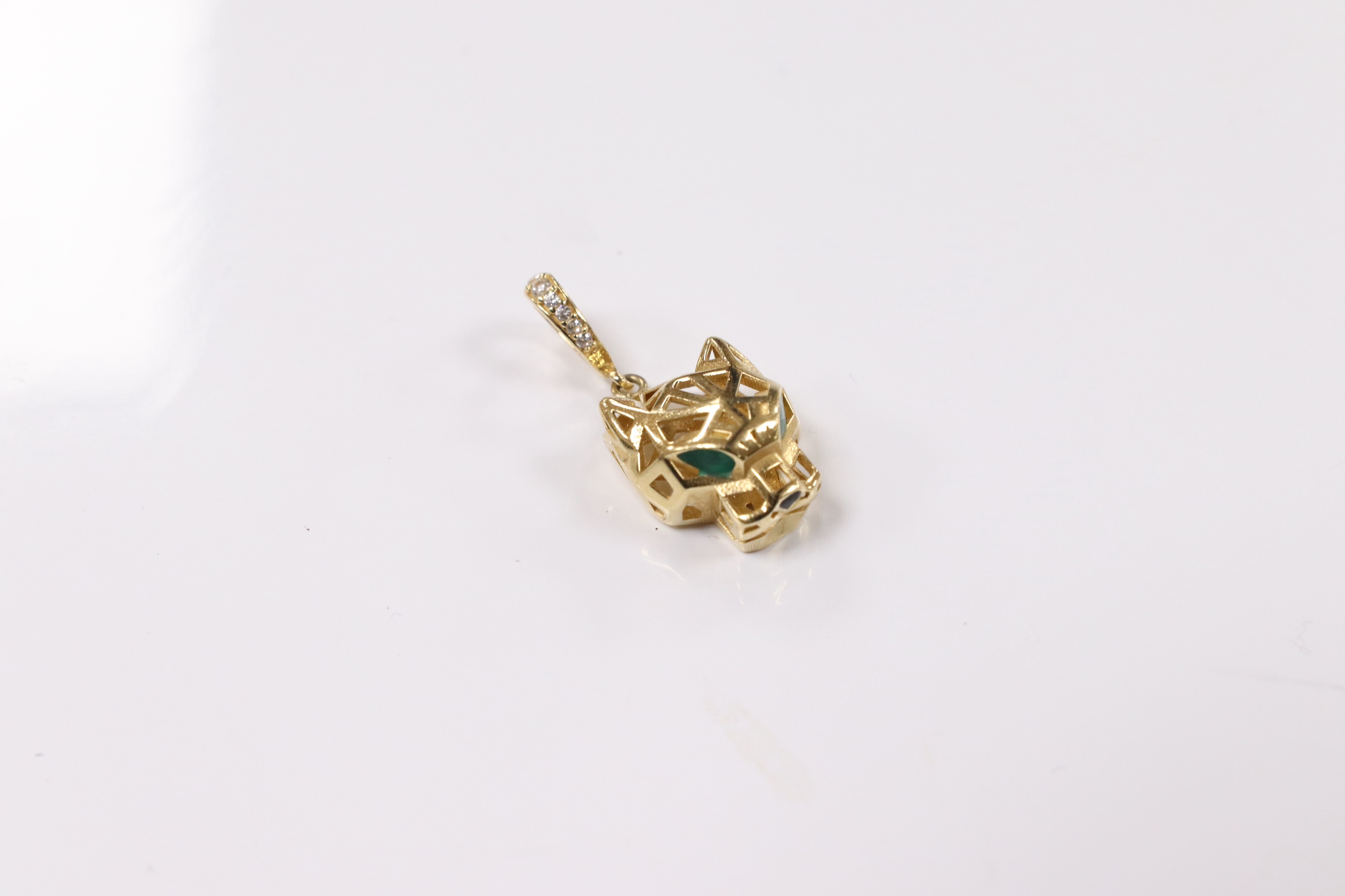 A modern Cartier style pierced 18k and emerald? set pendant, modelled as a leopard's head, with diamond chip set bale, overall 27mm, gross weight 2.5 grams. Condition - fair